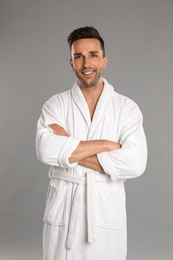 Happy young man in bathrobe on grey background