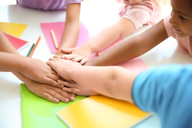 Photo of Little children putting their hands together at table, closeup. Unity concept