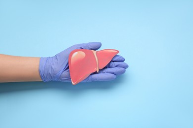 Photo of Doctor in glove holding paper liver on light blue background, closeup and top view. Hepatitis treatment