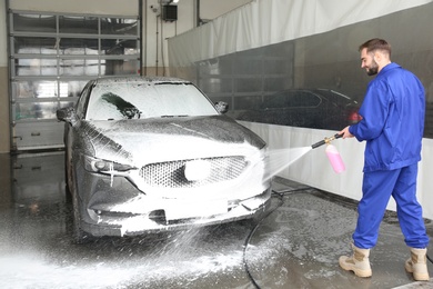 Worker cleaning automobile with high pressure water jet at car wash