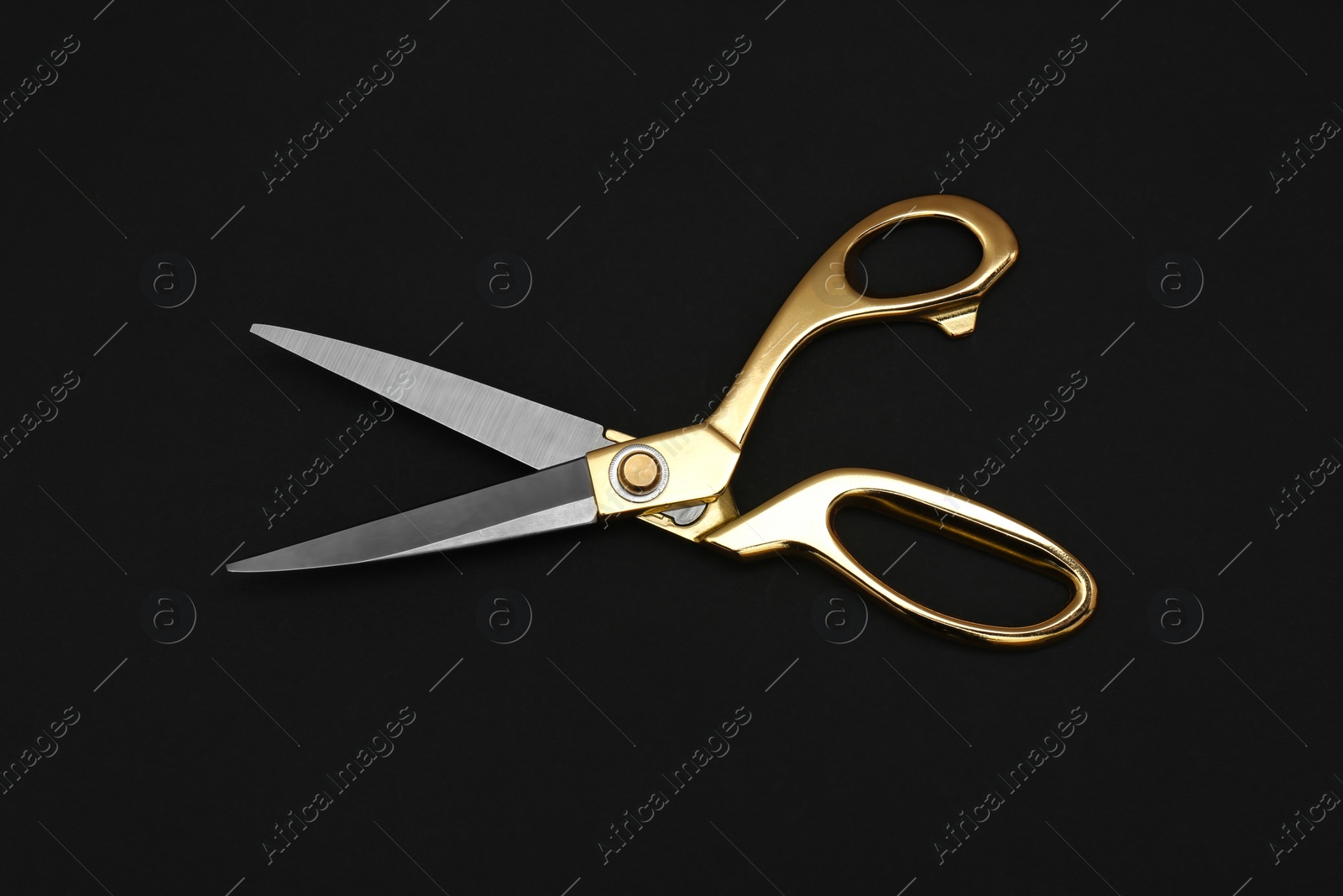 Photo of Gold tailor scissors on black background, top view