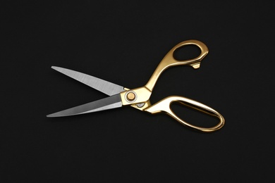 Photo of Gold tailor scissors on black background, top view