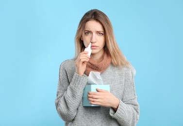 Photo of Sick young woman using nasal spray on light blue background