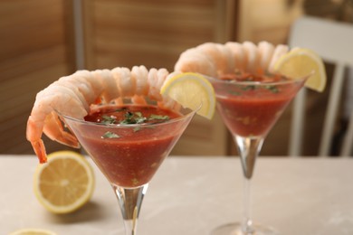 Photo of Tasty shrimp cocktail with sauce in glasses and lemon on light table, closeup