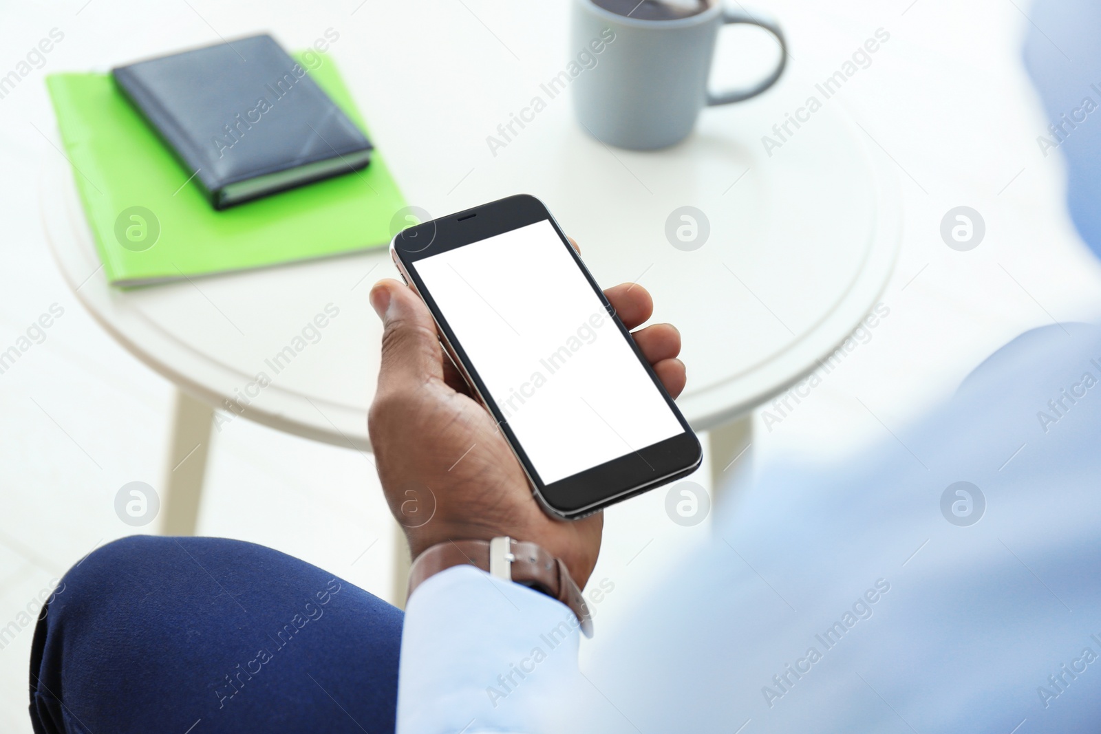 Photo of African-American man holding mobile phone with blank screen in hand indoors