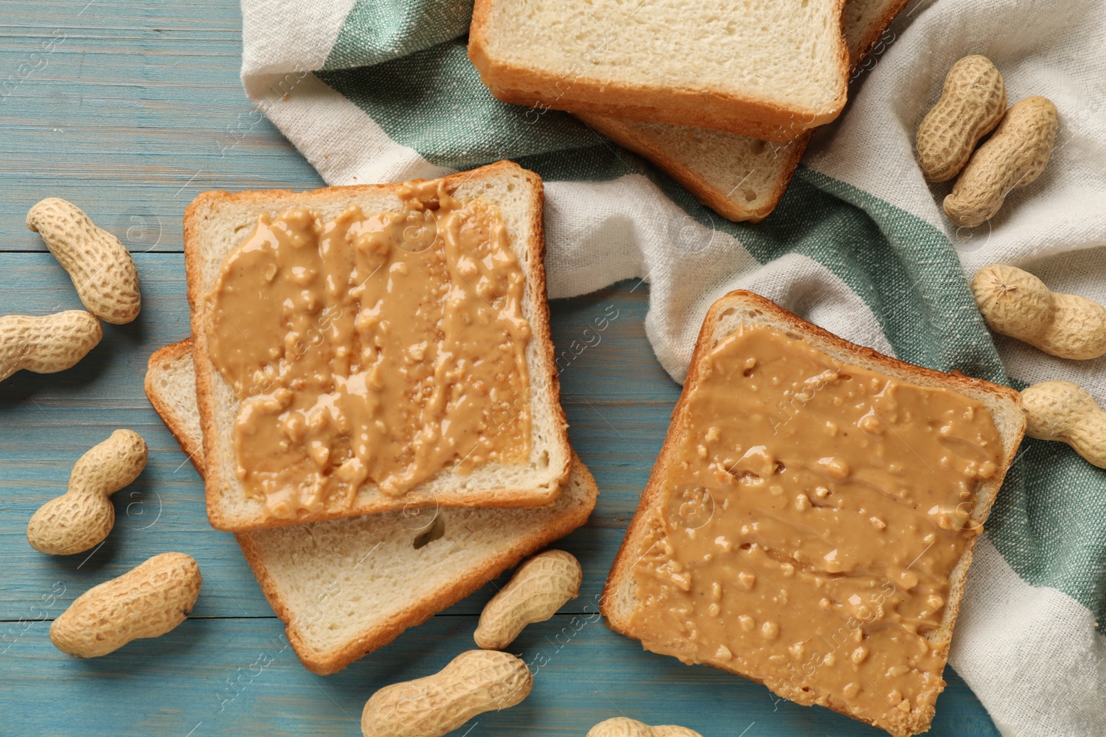 Photo of Delicious toasts with peanut butter and nuts on light blue wooden table, flat lay