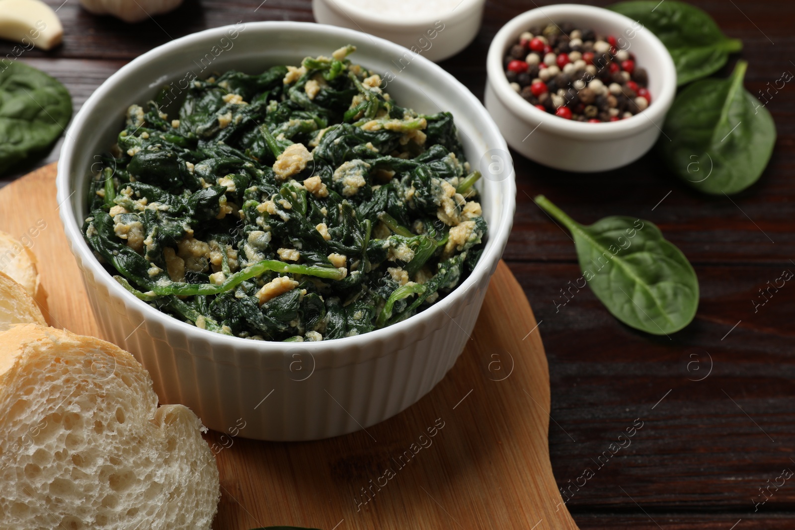 Photo of Tasty spinach dip with egg in bowl, bread and spices on wooden table, closeup