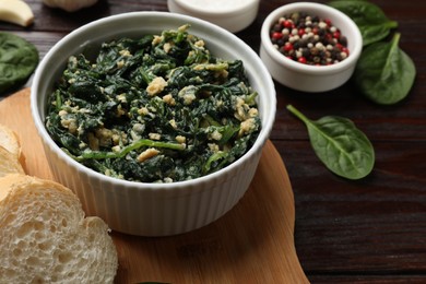 Photo of Tasty spinach dip with egg in bowl, bread and spices on wooden table, closeup