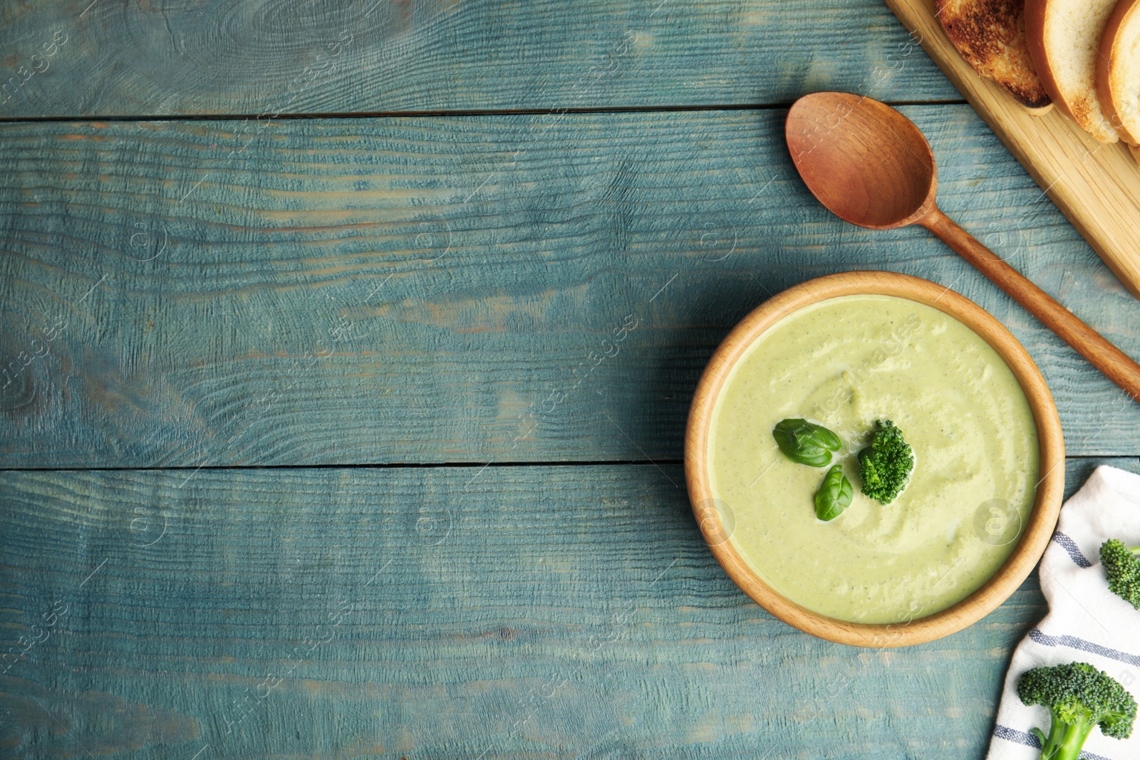 Photo of Delicious broccoli cream soup served on blue wooden table, flat lay. Space for text