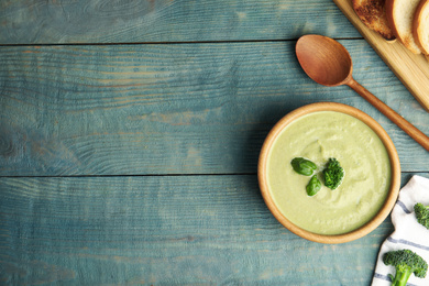 Photo of Delicious broccoli cream soup served on blue wooden table, flat lay. Space for text