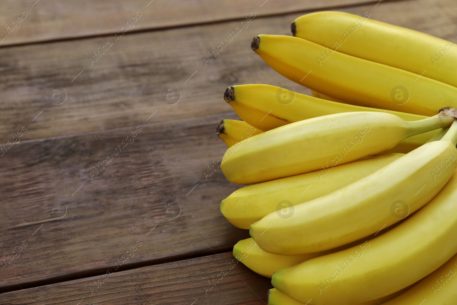 Photo of Ripe yellow bananas on wooden table, closeup. Space for text