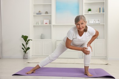 Happy senior woman practicing yoga on mat at home