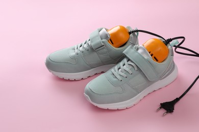 Photo of Pair of stylish sneakers with modern electric shoe dryer on pink background