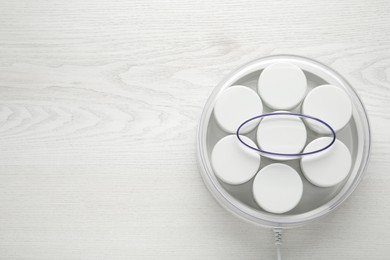 Modern yogurt maker with jars on white wooden table, top view. Space for text