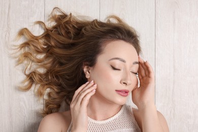 Photo of Portrait of beautiful woman with closed eyes on wooden floor, top view