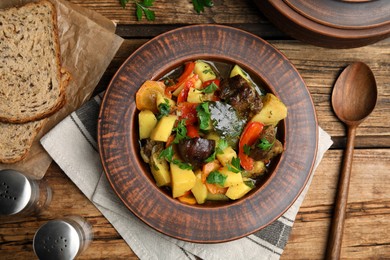 Photo of Tasty cooked dish with potatoes in earthenware served on wooden table, flat lay
