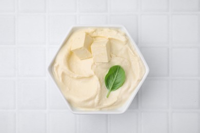 Photo of Delicious tofu sauce and basil leaf in bowl on white tiled table, top view