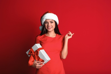 Photo of Young beautiful woman in Santa hat with gift box on color background. Christmas celebration