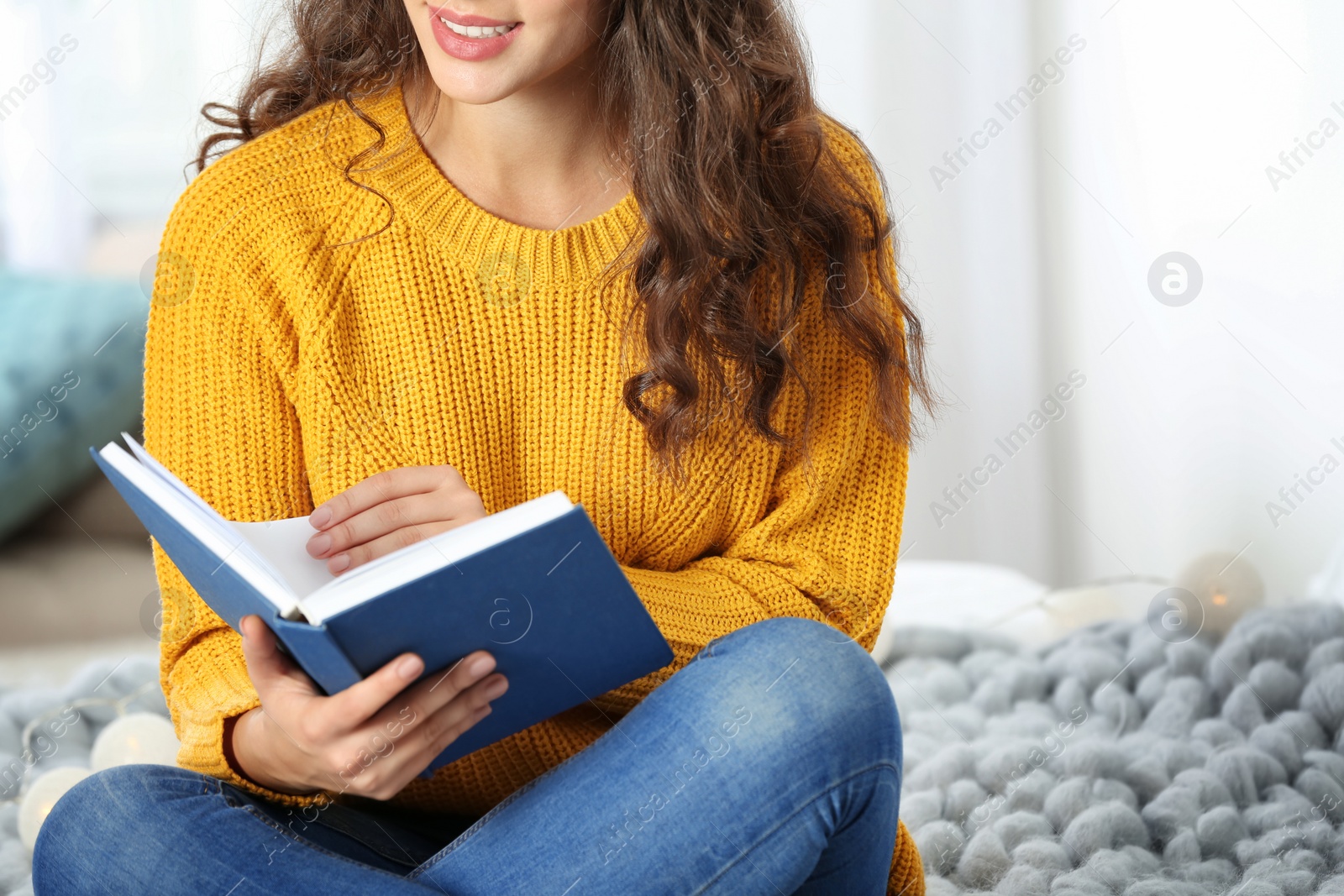 Photo of Young beautiful woman in warm sweater reading book on bed at home