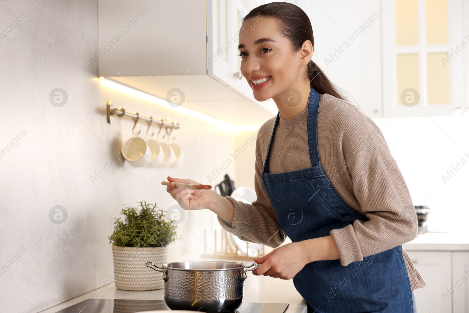 Photo of Smiling woman with wooden spoon tasting tomato soup in kitchen. Space for text