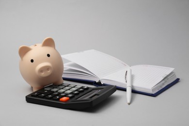 Calculator, piggy bank, pen and notebook on grey background