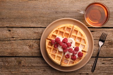 Photo of Tasty Belgian waffle with fresh raspberries, whipped cream, cup of tea and fork on wooden table, flat lay. Space for text