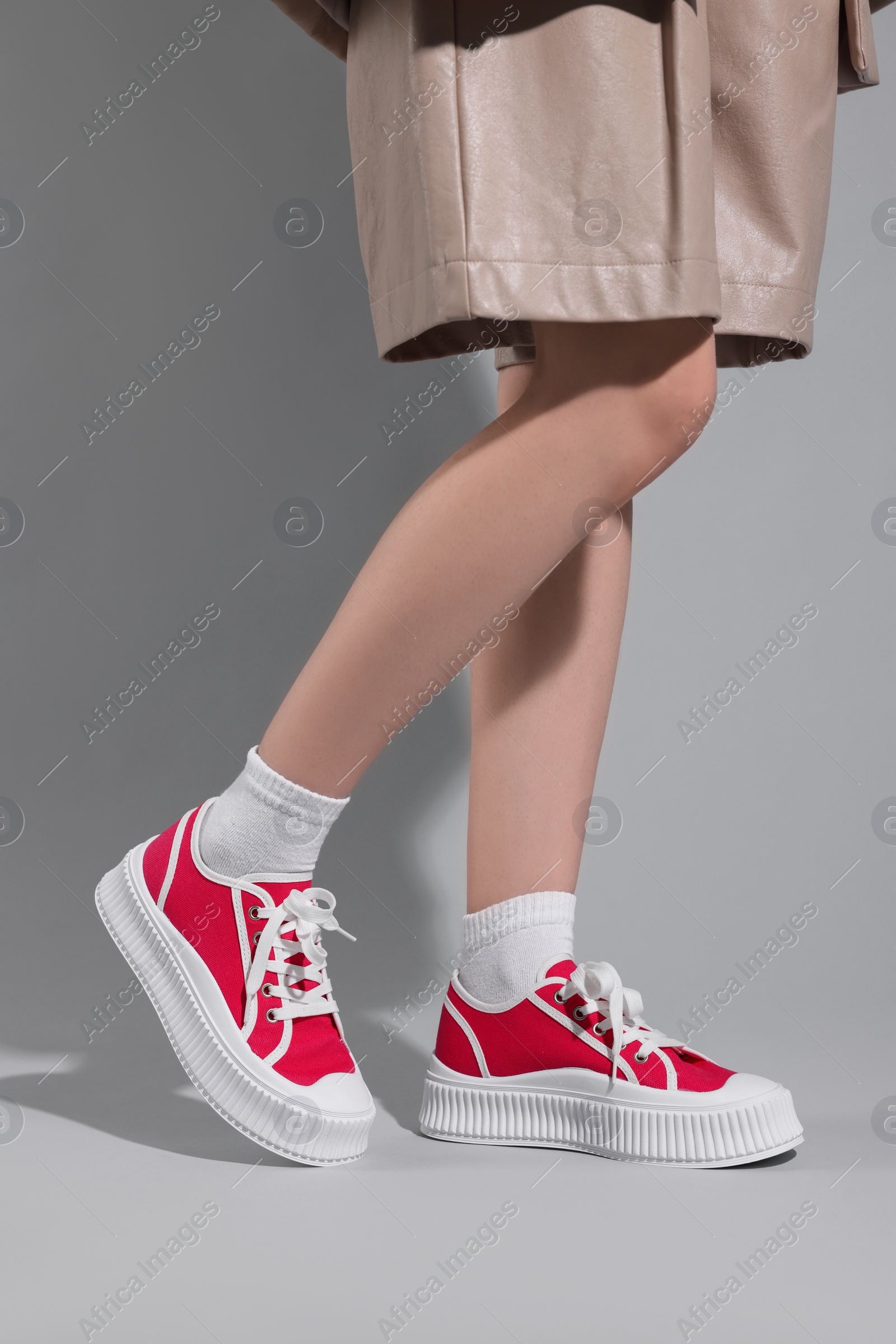 Photo of Woman wearing red classic old school sneakers on light gray background, closeup