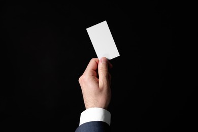 Photo of Businessman holding blank business card on black background, closeup