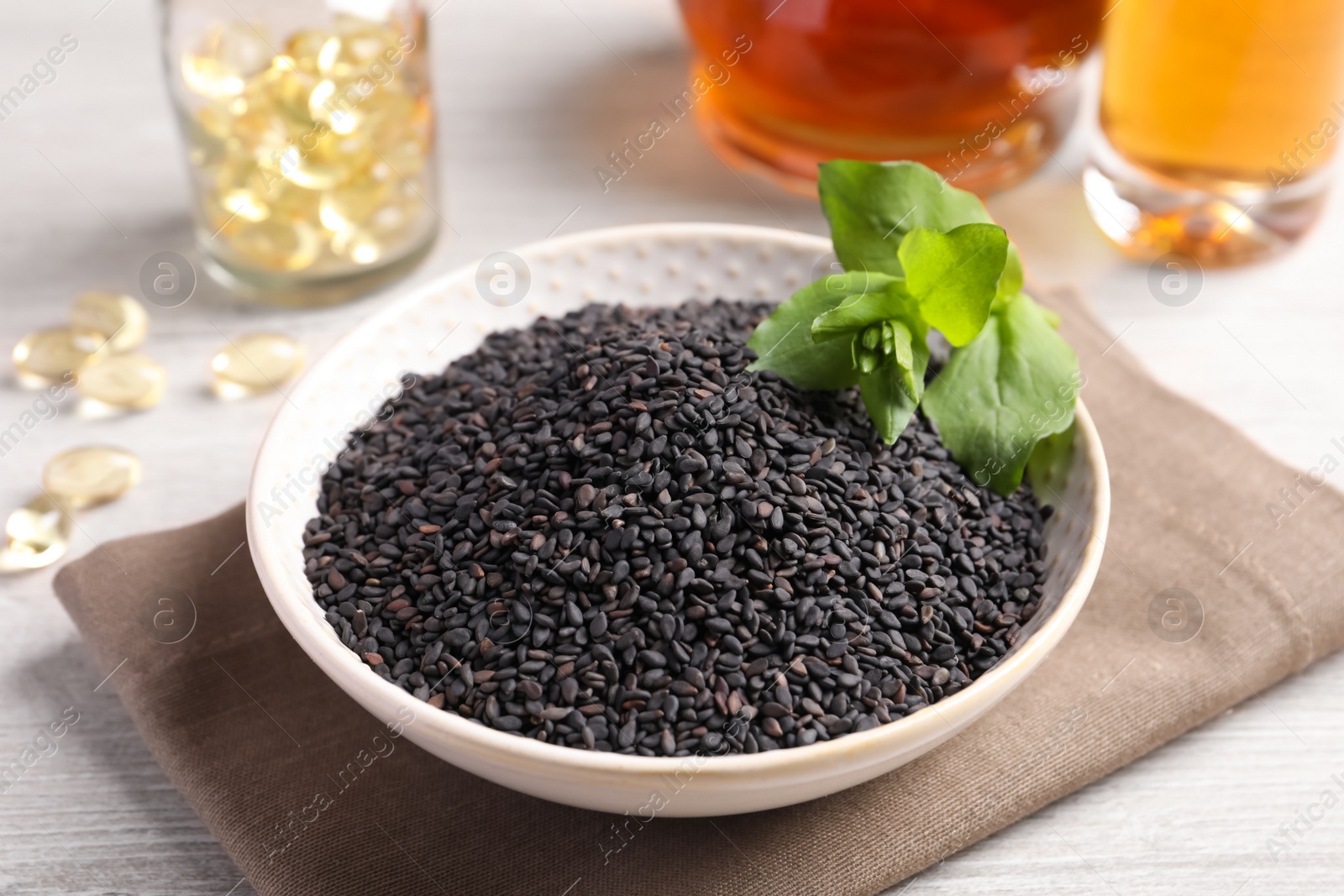 Photo of Black sesame seeds and green leaf in bowl on white wooden table, closeup