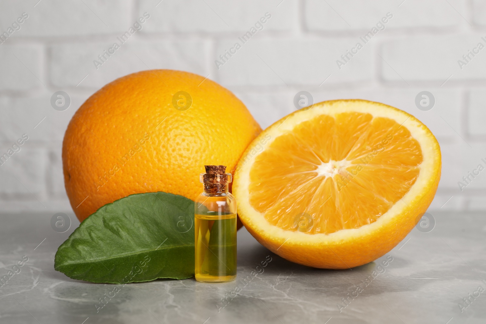 Photo of Bottle of essential oil with oranges and leaf on grey marble table against white brick wall
