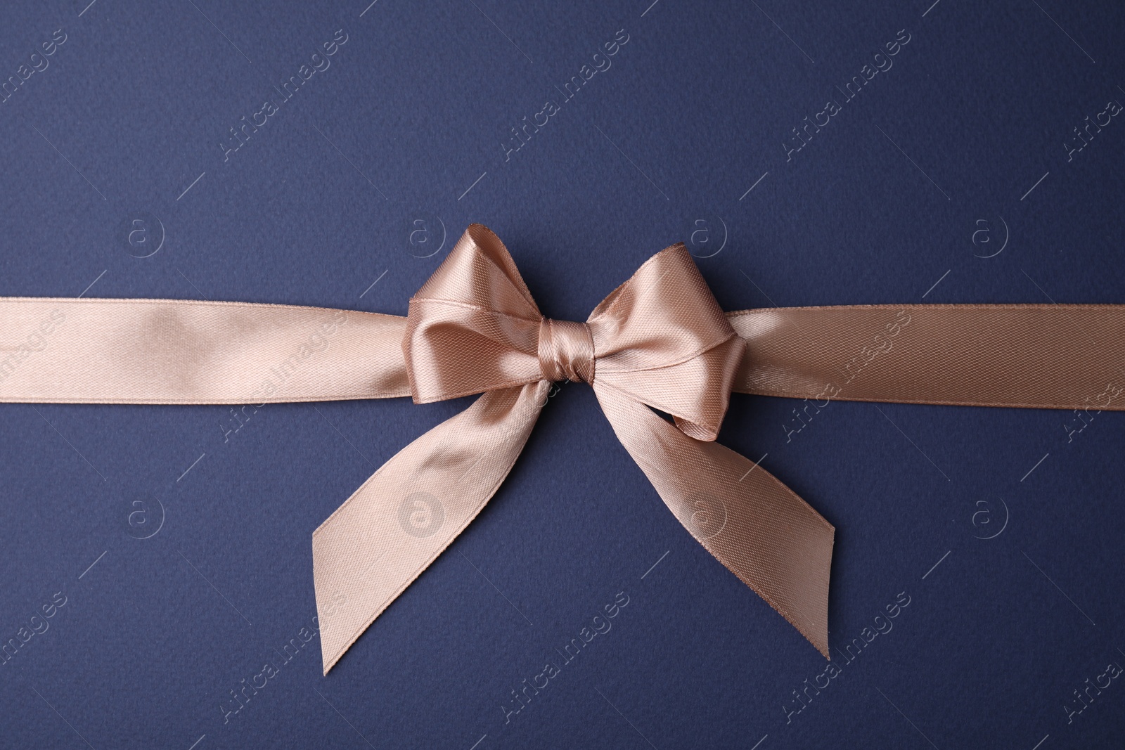 Photo of Beige satin ribbon with bow on blue background, top view