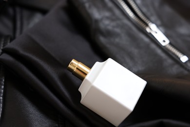 Photo of Bottle of perfume on black leather jacket, closeup