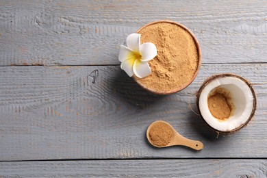 Coconut sugar, bowl, spoon, flower and fruit on grey wooden table, flat lay. Space for text