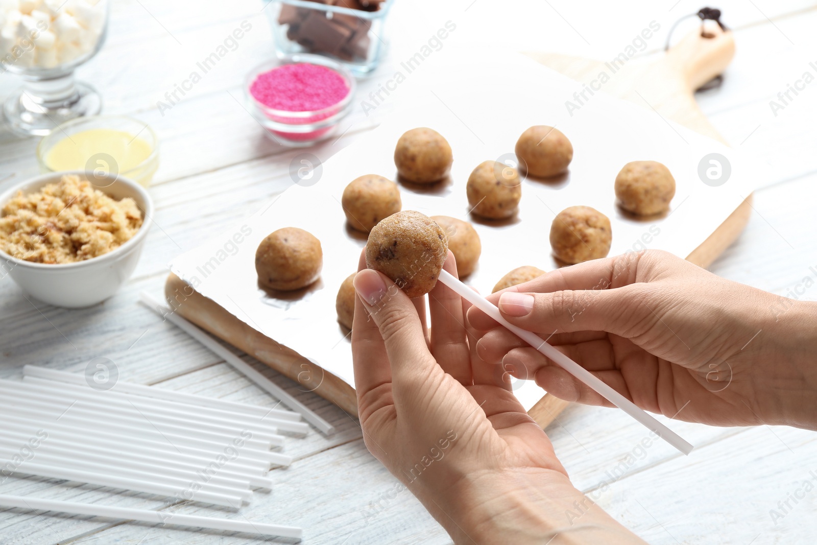 Photo of Woman making tasty cake pops at white wooden table, closeup