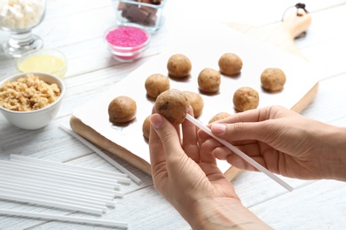 Photo of Woman making tasty cake pops at white wooden table, closeup