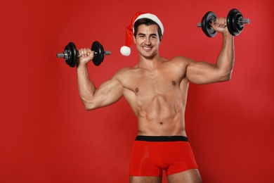 Photo of Sexy shirtless Santa Claus with dumbbells on red background