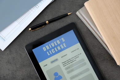 Tablet with driver's license application form and stationery on grey table, flat lay