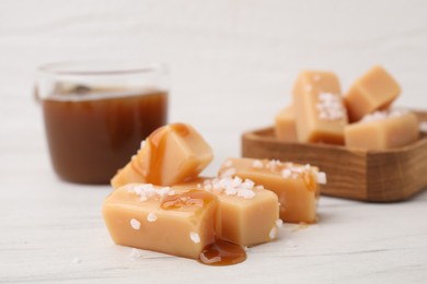 Yummy caramel candies, sauce and sea salt on white wooden table, closeup