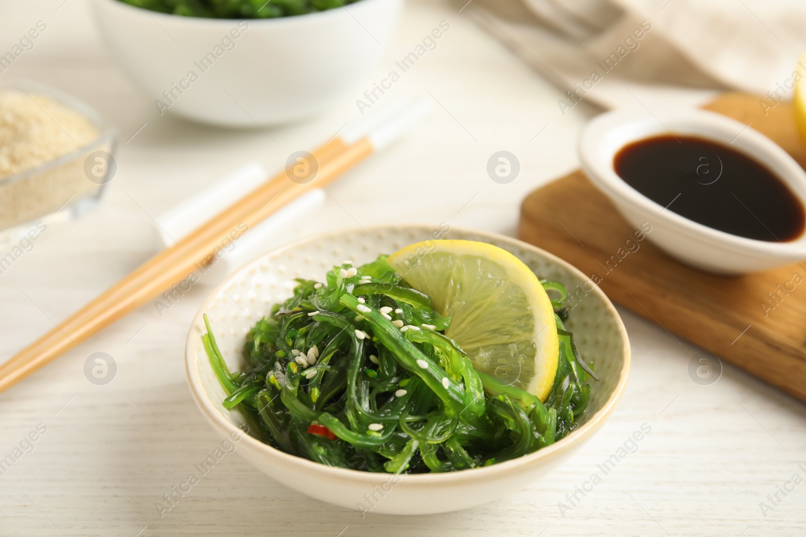 Photo of Japanese seaweed salad with lemon slice served on white wooden table, closeup