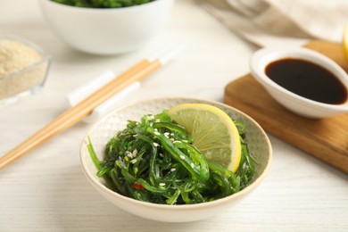 Photo of Japanese seaweed salad with lemon slice served on white wooden table, closeup