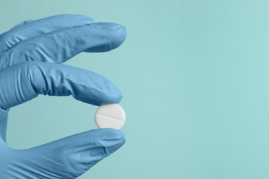 Doctor holding pill on turquoise background, closeup. Space for text
