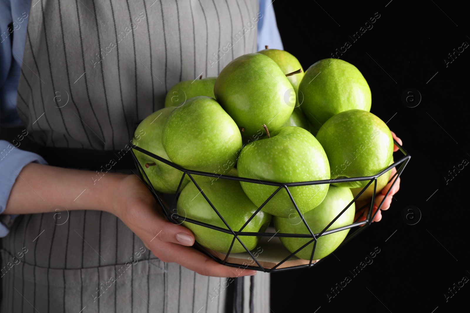 Photo of Woman holding fruit bowl with green apples against black background, closeup