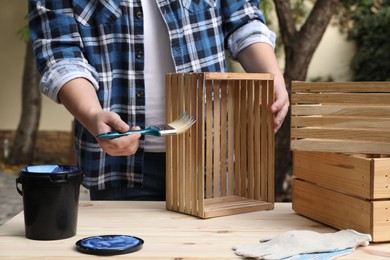 Photo of Man applying varnish onto wooden crate at table outdoors, closeup