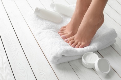 Woman with beautiful feet, towel and cosmetic products on white wooden floor, closeup. Spa treatment