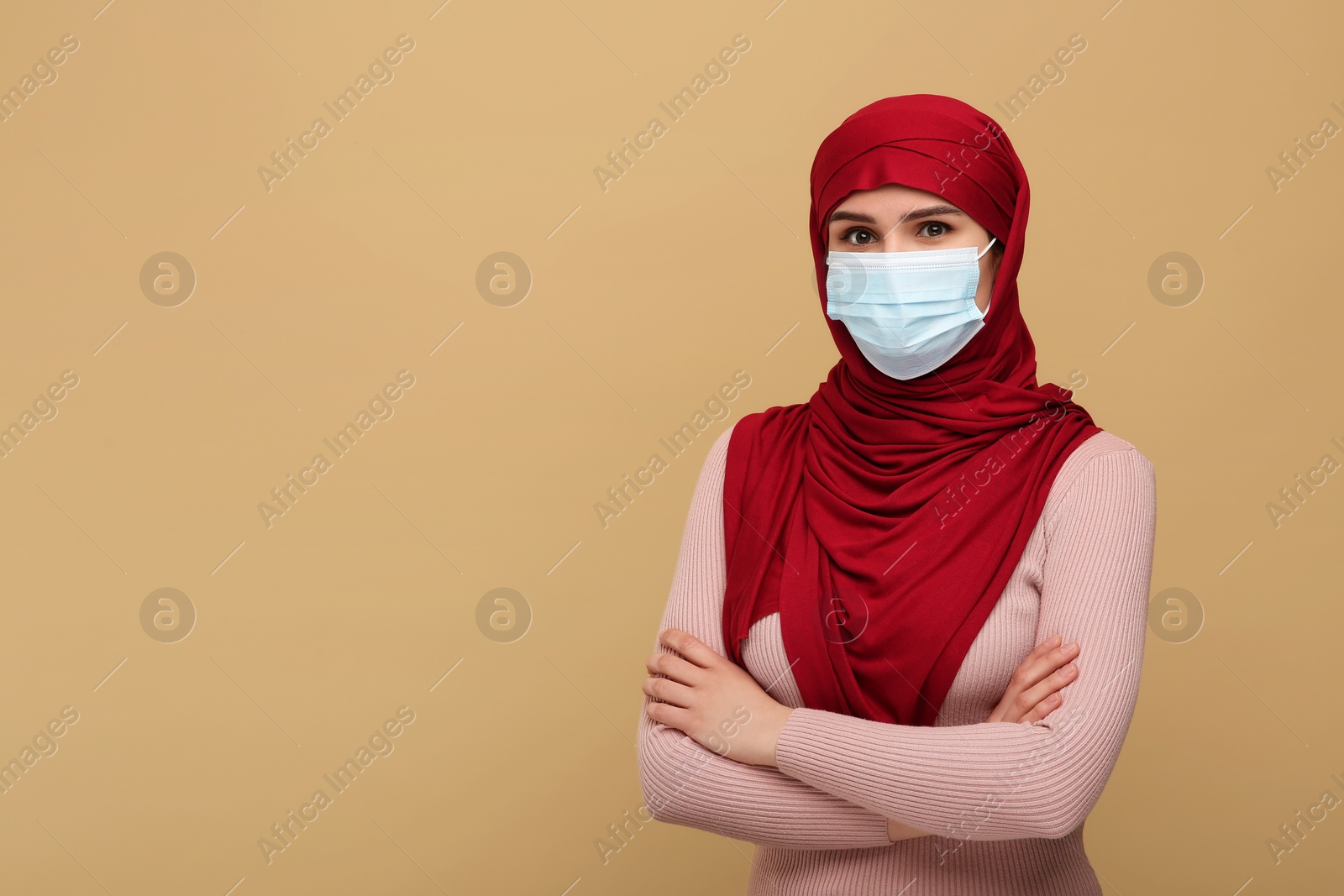 Photo of Muslim woman in hijab and medical mask on beige background, space for text