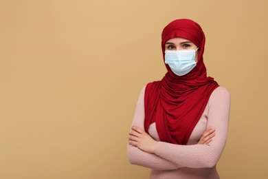 Muslim woman in hijab and medical mask on beige background, space for text