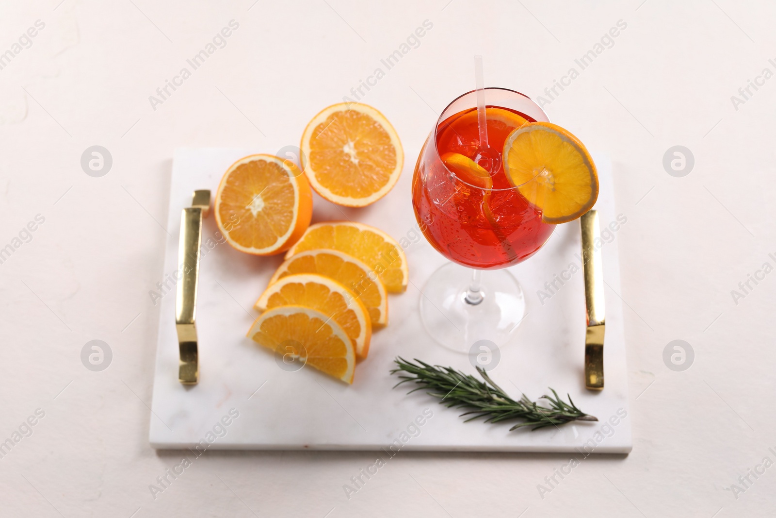 Photo of Glass of tasty Aperol spritz cocktail with orange slices and rosemary on white table, above view