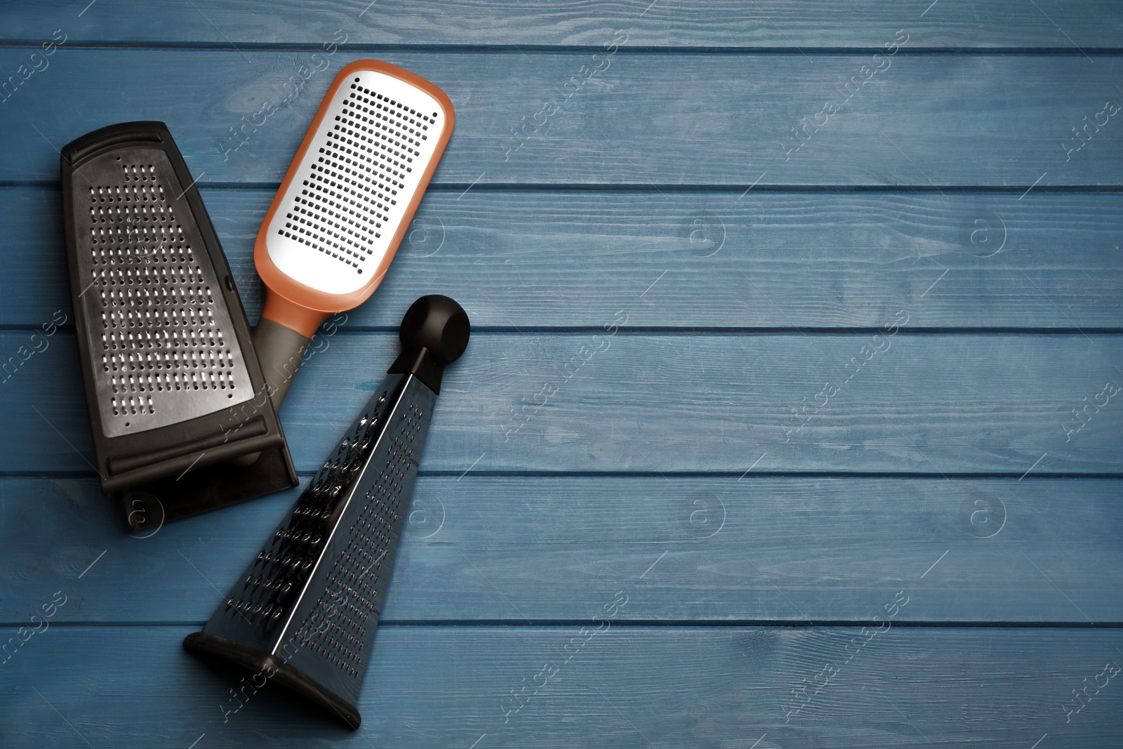 Photo of Different modern graters on blue wooden table, flat lay. Space for text