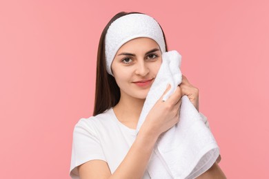 Washing face. Young woman with headband and towel on pink background