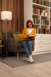 Photo of Beautiful young woman reading book in armchair indoors. Home library